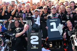 ​ماركو بيزيكي، خورخي مارتن، وأعضاء فريق "أبريليا" يرفعون رايات النصر احتفالاً بمنصة تتويج سباق جائزة البرازيل الكبرى للموتو جي بي.